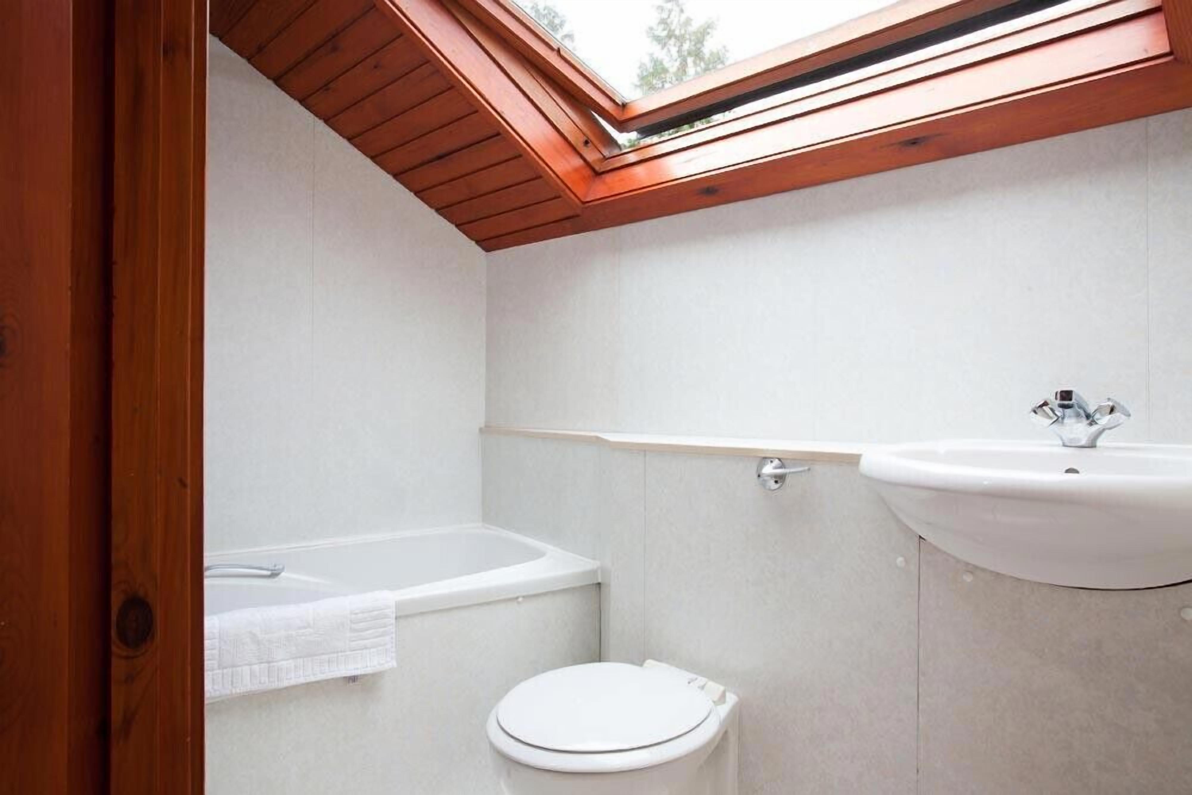 Un baño moderno con tragaluz, una bañera, un inodoro y un lavabo.