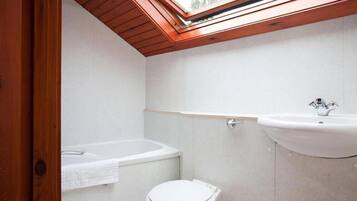 Un baño moderno con tragaluz, una bañera, un inodoro y un lavabo.