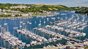 A marina filled with numerous boats docked in a harbor surrounded by a town and green hills. - George Cottage (Dartmouth)