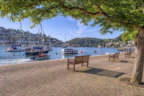 A waterfront promenade with benches, a tree, and boats docked along the shore. - George Cottage (Dartmouth)