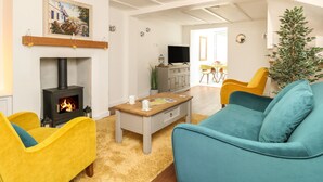 A living room with a fireplace, yellow and blue chairs, a coffee table, and a television.