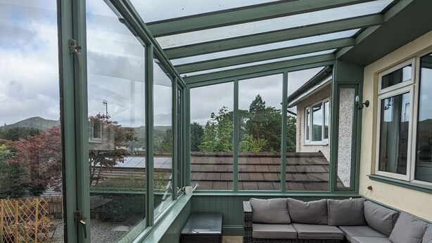 Une véranda dotée d’un toit en verre, un canapé, une petite table et une vue sur une colline et un plan d’eau.