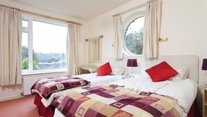 Une chambre avec deux lits, une fenêtre avec des rideaux, un miroir rond et une table de chevet avec une lampe.