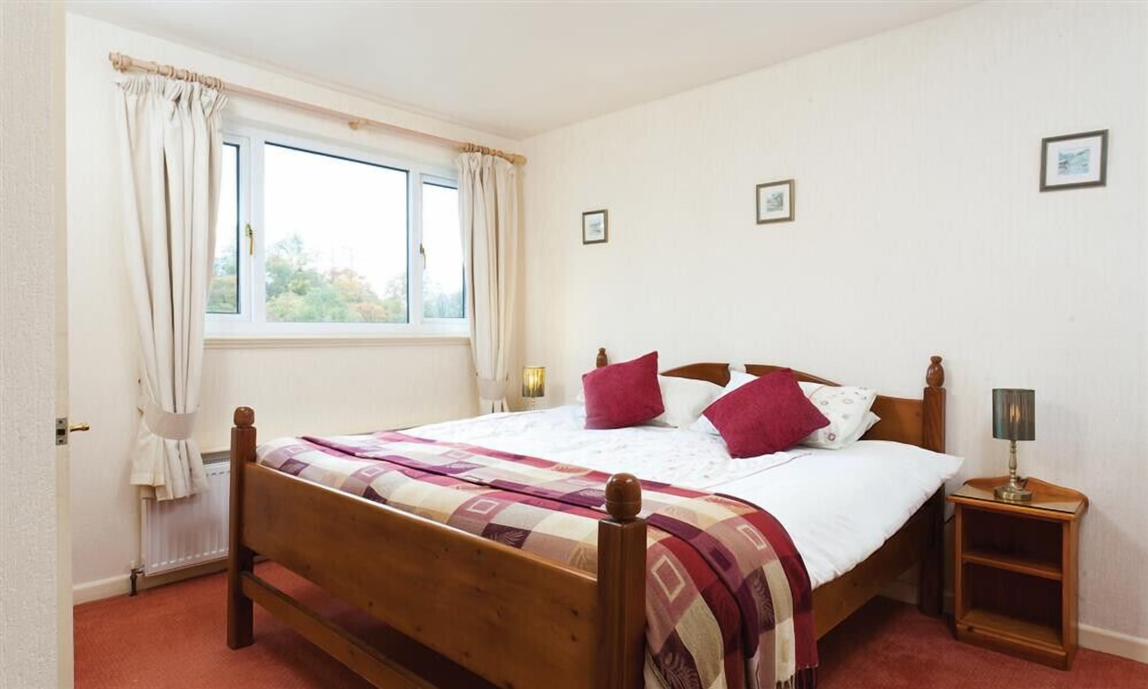 Une chambre à coucher avec un lit en bois, une fenêtre avec des rideaux, une table de chevet avec une lampe, et deux tableaux encadrés accrochés au mur.