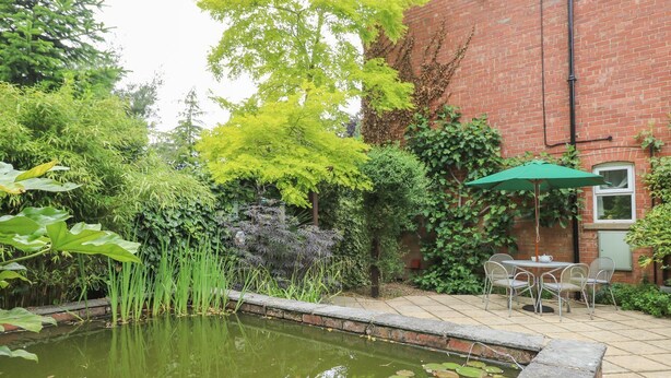 A garden with a pond, a brick building, and outdoor seating. - Lansdowne Lodge (Market Rasen)