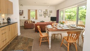 A modern kitchen with wooden cabinets, a dining area with a wooden table and chairs, a brown leather sofa, and a TV in the living room. - Lansdowne Lodge (Market Rasen)