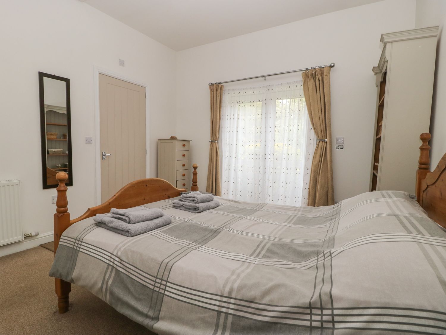 Un dormitorio con cama de madera, cómoda, espejo y ventana con cortinas.