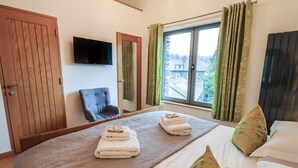 Une chambre à coucher avec un grand lit, une armoire en bois, une chaise, un téléviseur et une fenêtre avec des rideaux.