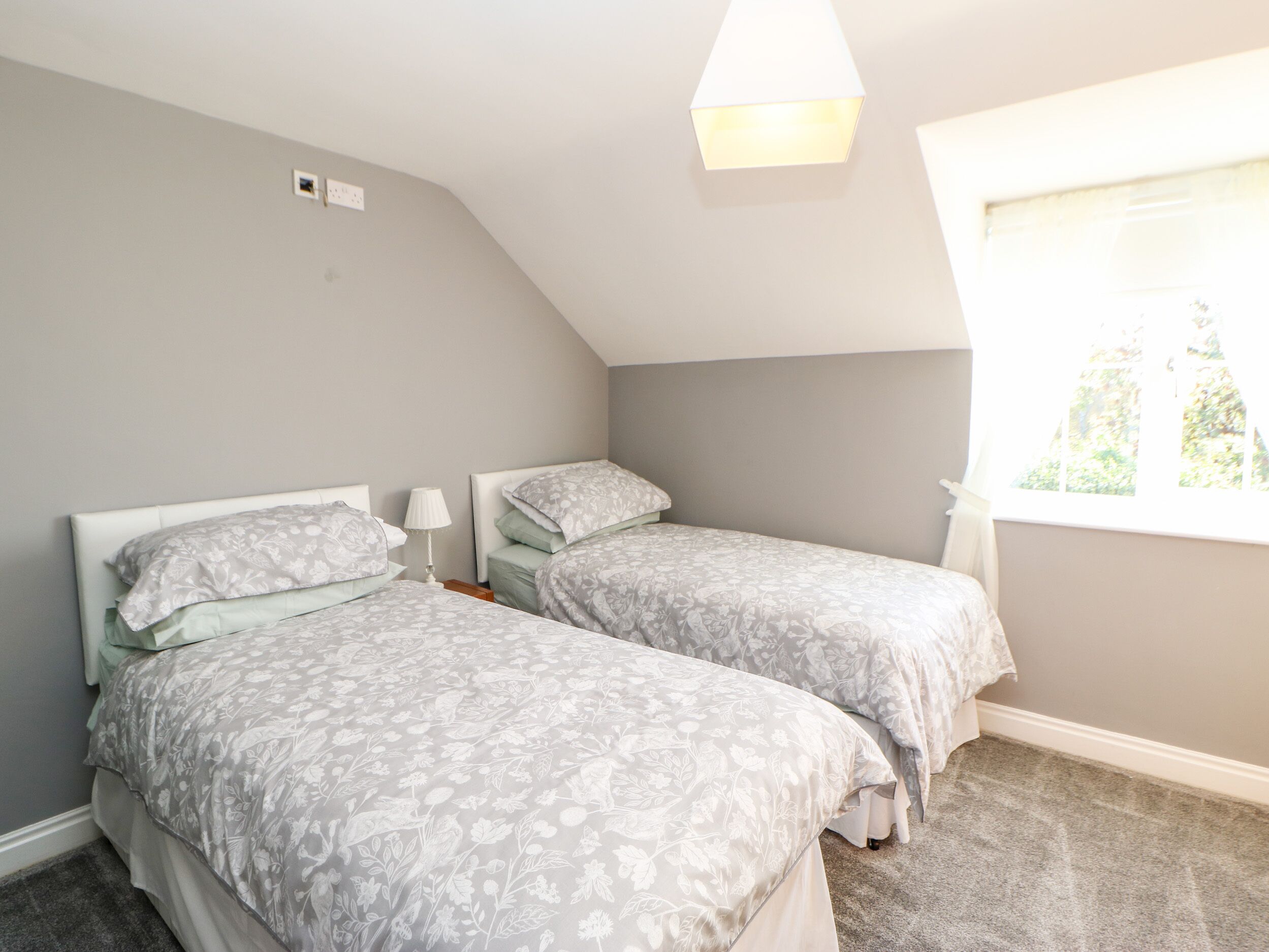 Un dormitorio con dos camas individuales, una ventana con persianas, una lámpara de techo y una mesita de noche con lámpara.
