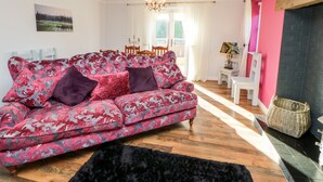 Sala de estar com sofá estampado, tapete preto, piso de madeira, lustre e área de jantar com cadeiras e mesa.
