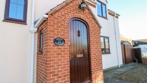 Uma casa de tijolos com porta de madeira escura, um pequeno alpendre e uma placa com a inscrição 'ANVIL COTTAGE'.