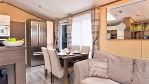 A modern kitchen with a built-in refrigerator, a dining table set for four, and a sofa in the living area. - Lancashire Rose (Windermere)