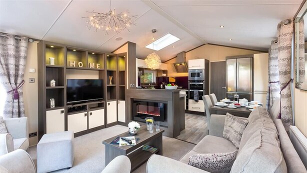 A modern living room with a flat-screen TV, comfortable seating, a fireplace, and a kitchen area visible through an open door. - Lancashire Rose (Windermere)