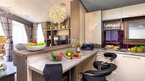 A modern kitchen with a central island, bar stools, a built-in wine cooler, and a view of the living area. - Lancashire Rose (Windermere)