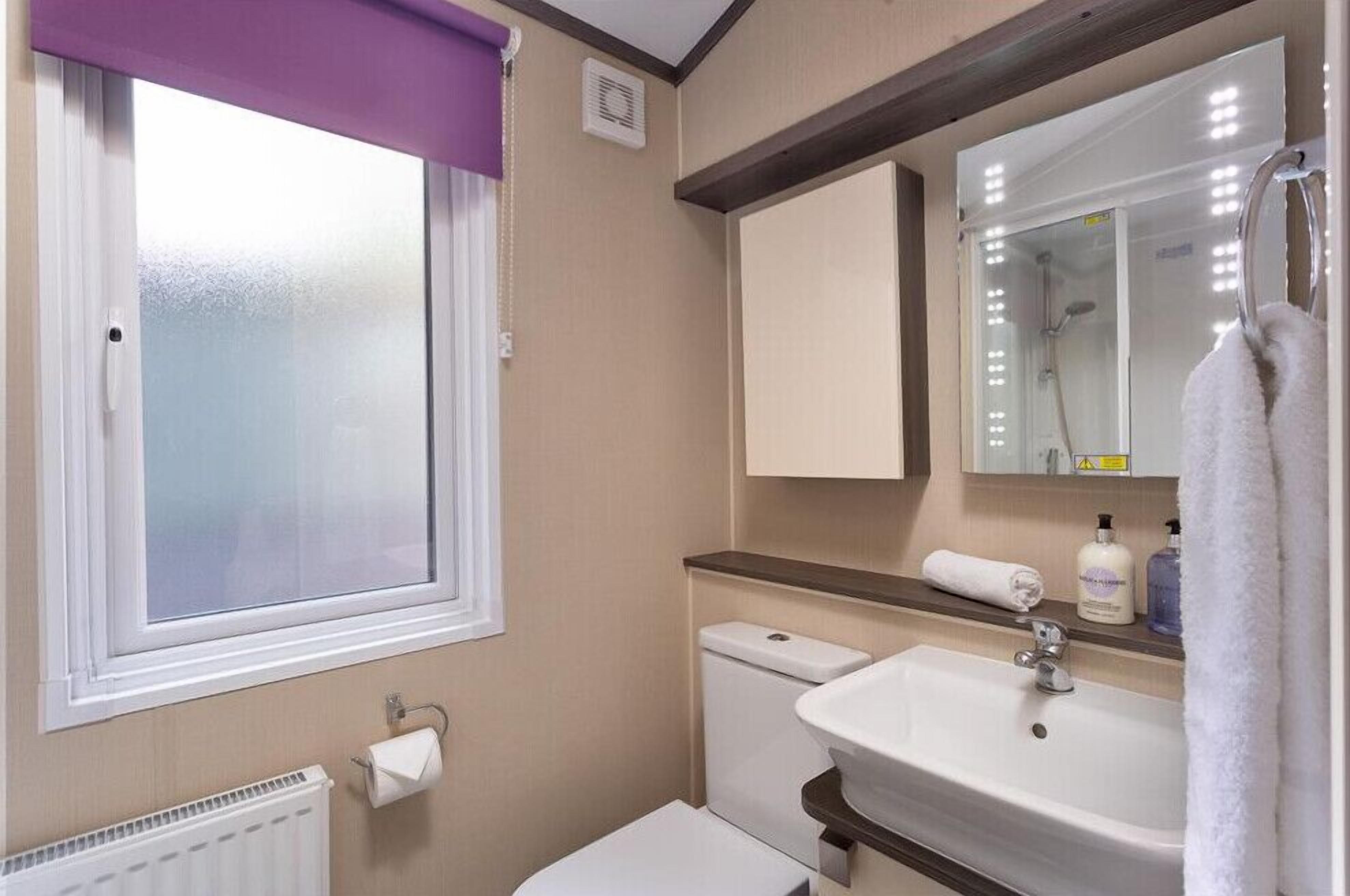 Une salle de bain avec une fenêtre, des toilettes, un lavabo et un miroir.