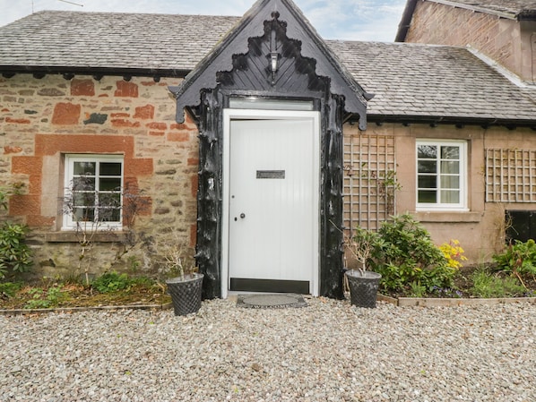 A stone building with a white door, a small window, and a gravel driveway. - Ellanderroch (Drymen)