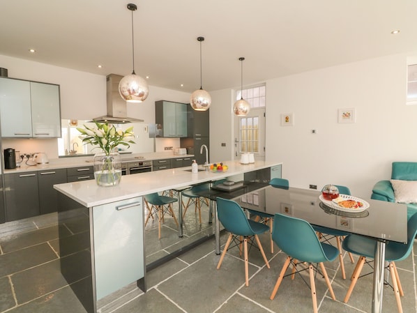 A modern kitchen with a central island, teal chairs, and pendant lighting.