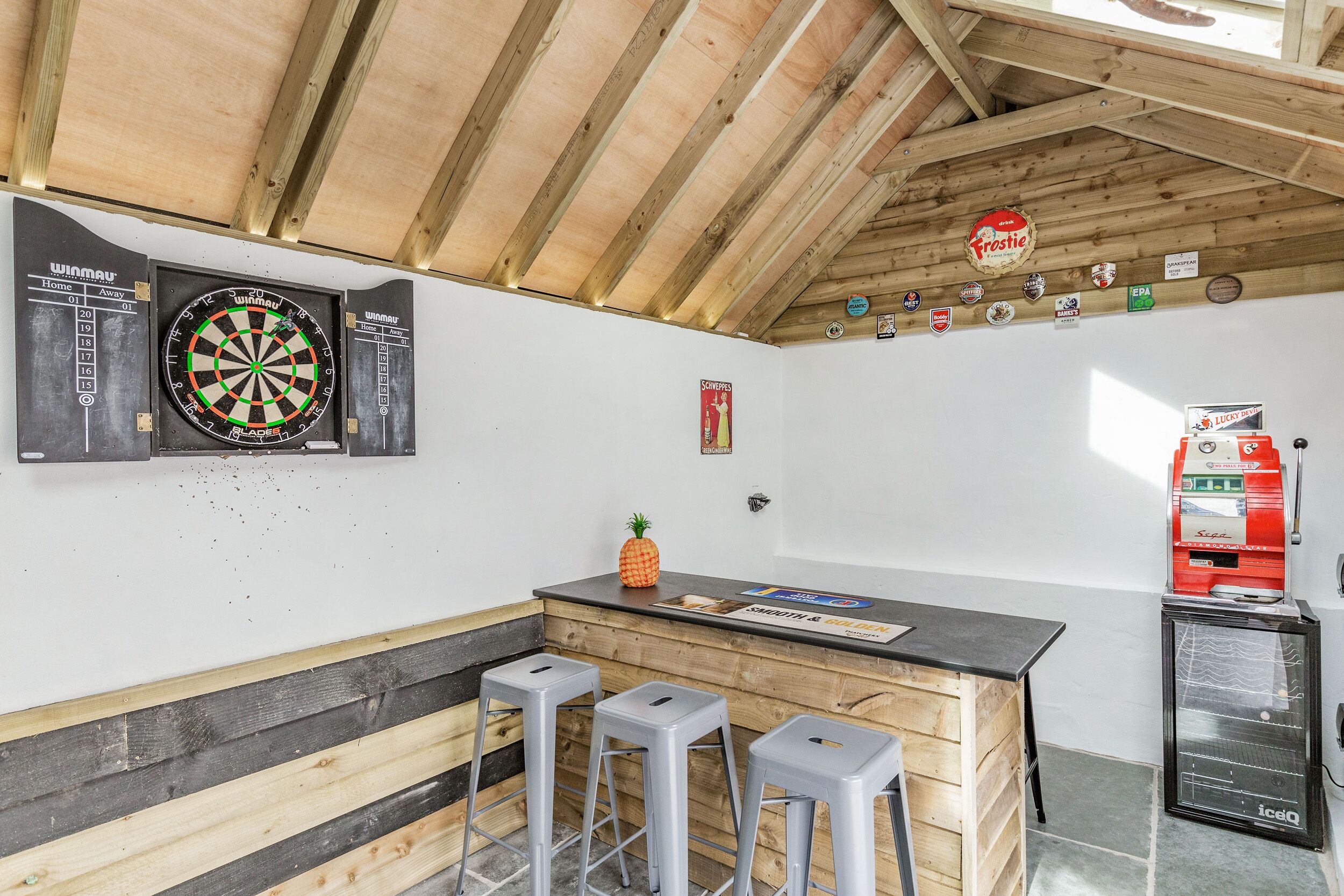 Zona de bar con dardos, taburetes, un refrigerador y un congelador.