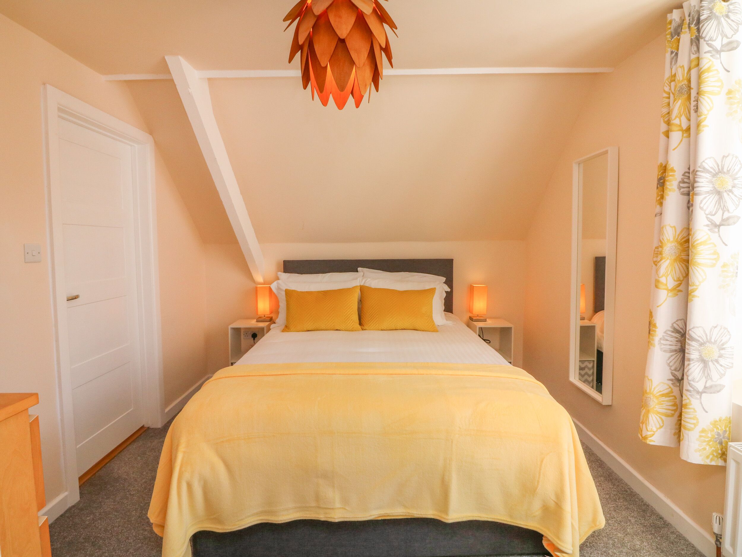 A bedroom with a bed, two bedside tables, a nightstand, a mirror, and a ceiling fan.