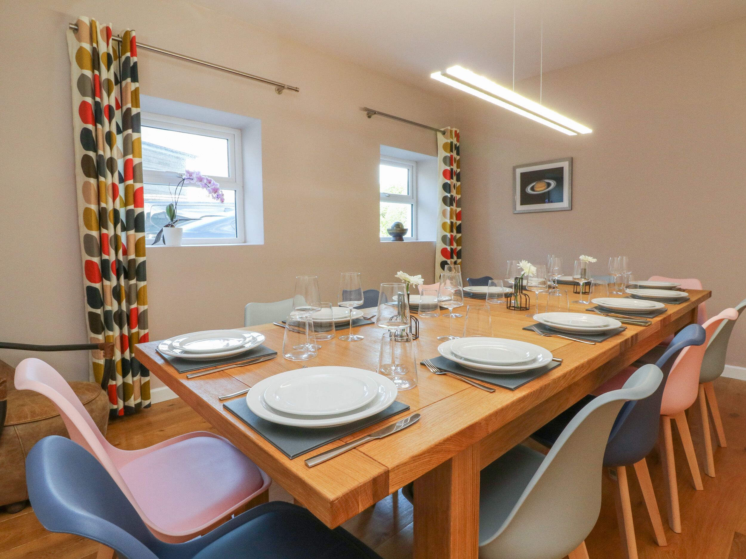 A dining area with a long wooden table set for a meal, surrounded by colorful chairs.