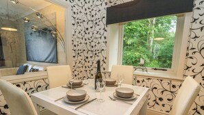 Un comedor con una mesa preparada para dos personas, una botella de vino y vistas a la vegetación a través de una ventana.