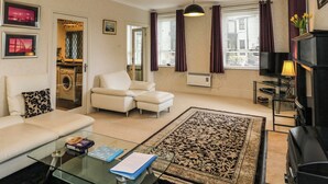 Una sala de estar con sofá, sillones, una mesa de centro de vidrio, televisor y chimenea.