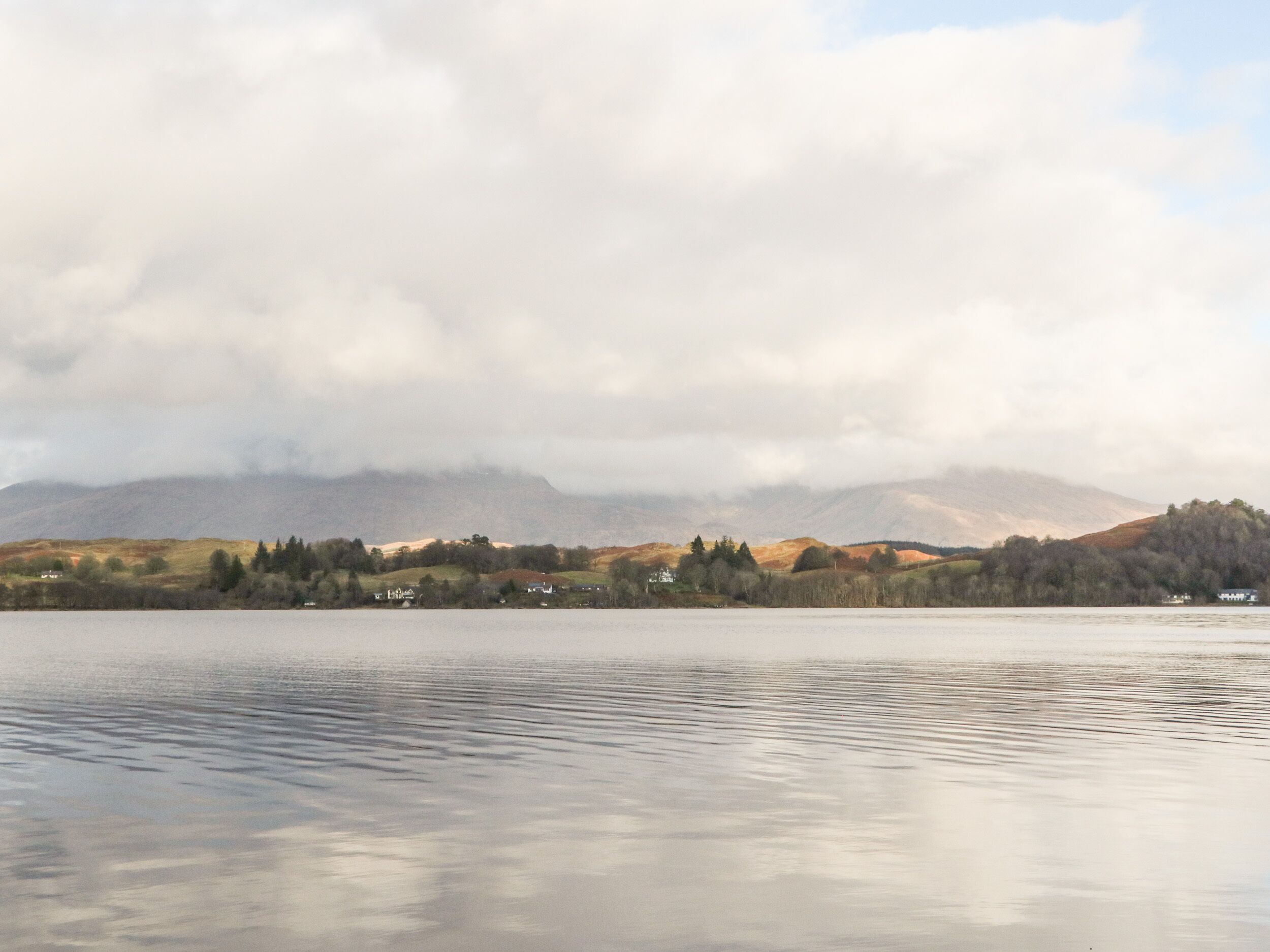 A calm lake with a village and mountains in the background.