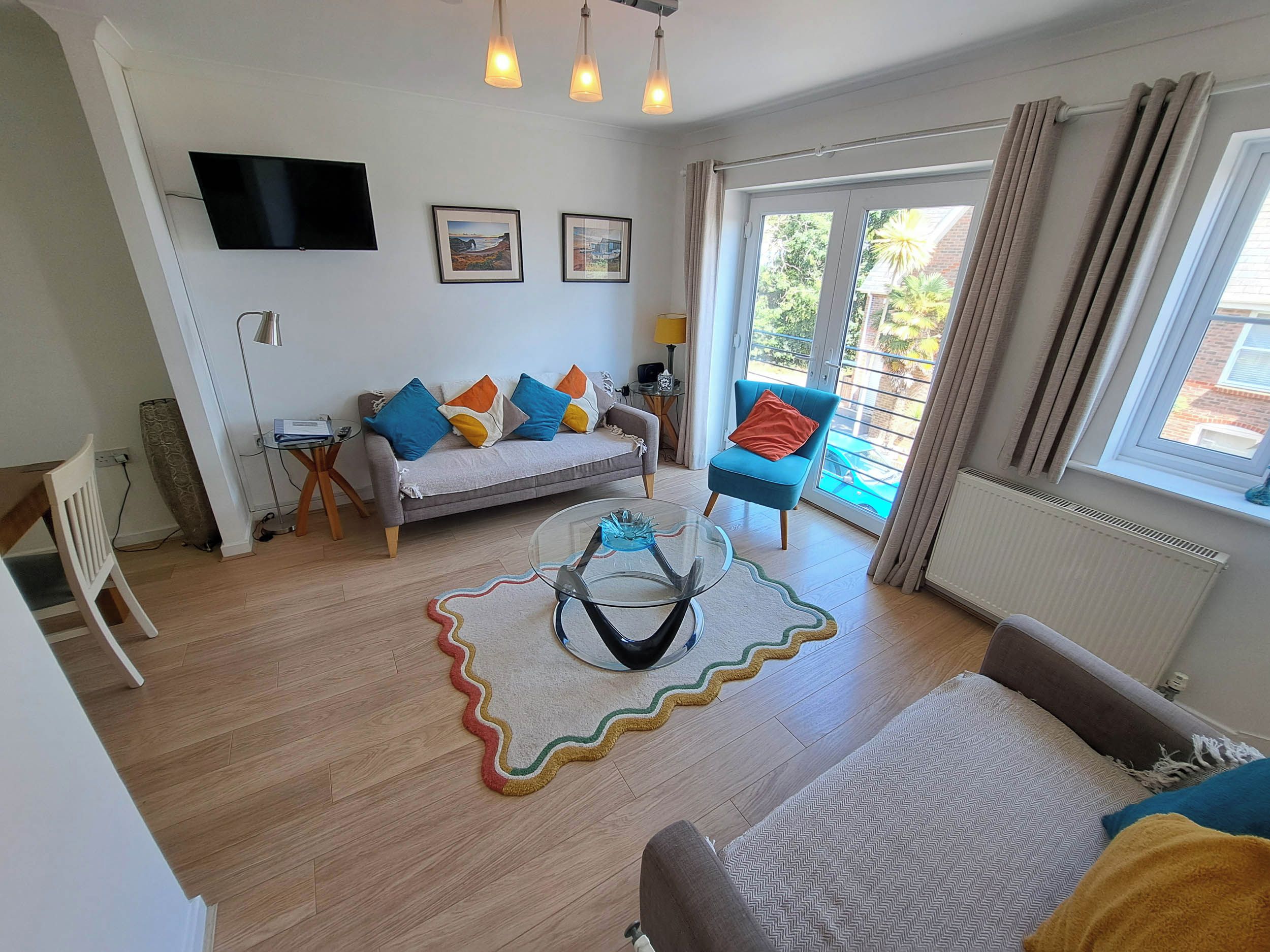 Un salon comprenant un canapé, une table basse, un téléviseur fixé au mur et une grande fenêtre avec des rideaux.
