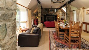 Una sala de estar acogedora con una pared de piedra, una chimenea, un rincón de comedor con sillas de madera y una mesa, y un sofá de cuero.