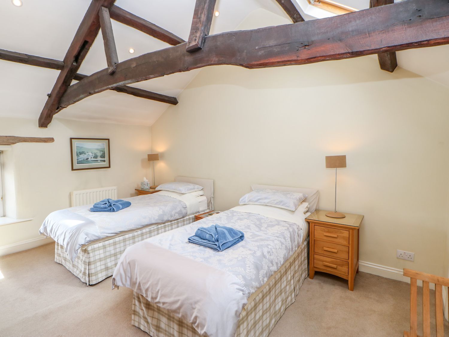 A bedroom with two beds, a wooden nightstand, a lamp, and a window.