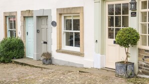 A row of traditional white buildings with distinct doorways and windows, a cobblestone street, and a small potted plant in front of one building. - Demonicus (Leyburn)