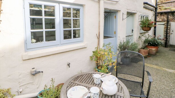 A patio with a table set for tea, a chair, and potted plants. - Demonicus (Leyburn)