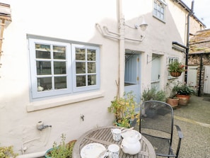 A courtyard with a table set for tea, a chair, and potted plants. - Demonicus (Leyburn)