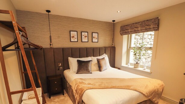 A bedroom with a bed, a wooden ladder, a nightstand, a window with a view, and three framed pictures on the wall. - Durham Bridge Barn (Kendal)