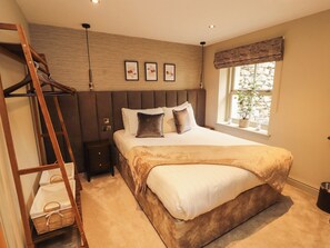 A bedroom with a bed, a wooden ladder, a nightstand, a window with a view, and three framed pictures on the wall.