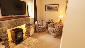 A living room with a stone fireplace, a television mounted above it, two patterned armchairs, a rug, and a framed picture on the wall. - Durham Bridge Barn (Kendal)