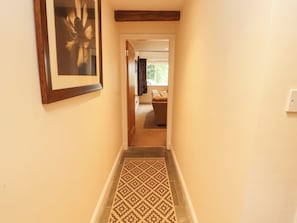 A hallway with a patterned carpet, a framed picture on the wall, and a doorway leading to a room with a couch.