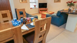 Una sala de estar acogedora con una mesa de comedor de madera, un sofá azul y un televisor.