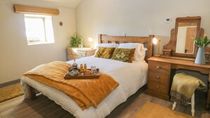A bedroom with a bed, bedside table, dresser, and a window. - The Hayloft (Holmfirth)