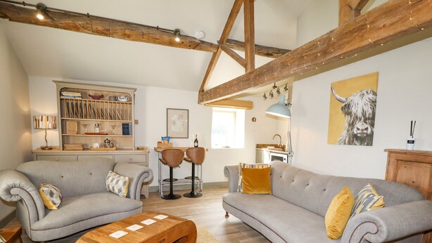 A spacious living area with two sofas, a wooden coffee table, and a kitchen in the background. - The Hayloft (Holmfirth)