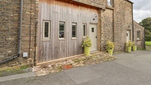 A stone building with a large wooden garage door, a small window, and three potted plants in front. - The Hayloft (Holmfirth)