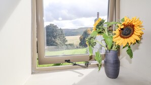A window with a view of a rural landscape, a vase with sunflowers, and a curtain rod. - The Hayloft (Holmfirth)