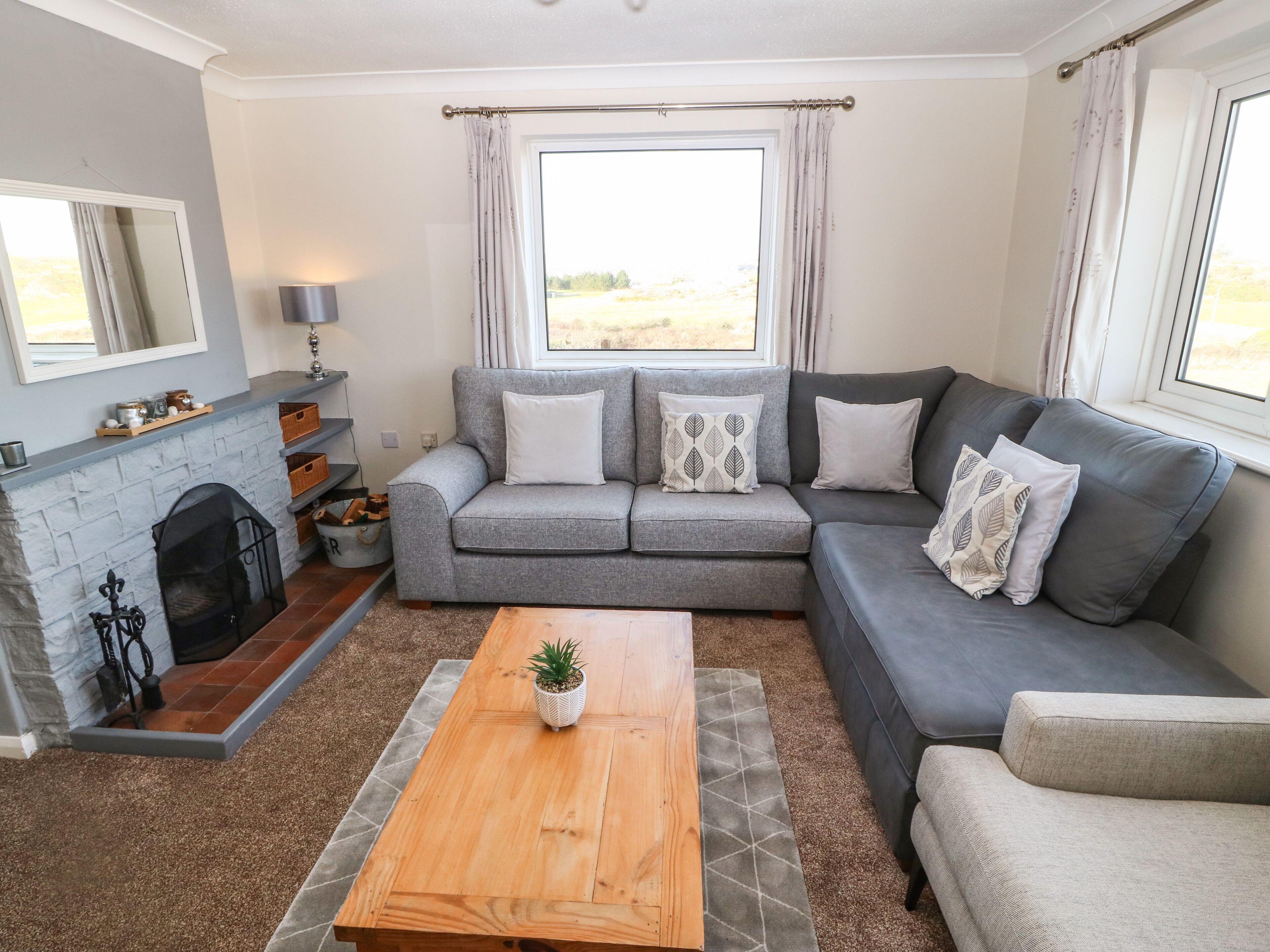 A living room with a grey sofa, a wooden coffee table, a fireplace, and a window with curtains.