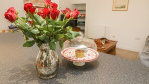 Un comptoir de cuisine orné d’un vase de roses rouges, recouvert d’une cloche en verre, et sur lequel est posée une assiette avec un cupcake.
