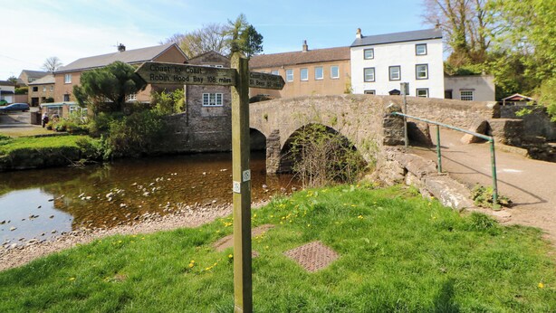 Un pont de pierre enjambant une rivière, avec un panneau indicateur indiquant les directions vers Robin Hood Bay et St Bees.
