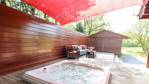 A hot tub in a wooden deck area with a wooden fence and a small wooden structure in the background. - Gisburn Forest Lodge (Skipton)
