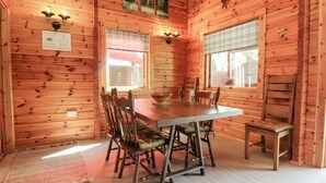 A wooden cabin interior with a dining table, chairs, and a fireplace. - Gisburn Forest Lodge (Skipton)
