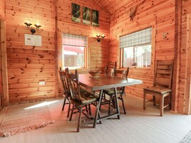 Interior de uma cabana de madeira com uma mesa de jantar, cadeiras e lareira.