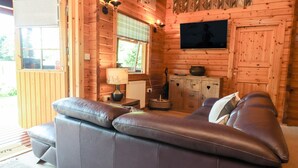 A log cabin interior with a leather sofa, a television mounted on the wall, and a rustic decor. - Gisburn Forest Lodge (Skipton)