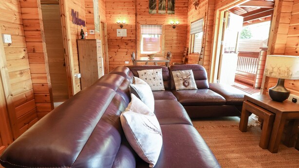 A log cabin interior with a leather sofa, wooden walls, and a dining area. - Gisburn Forest Lodge (Skipton)